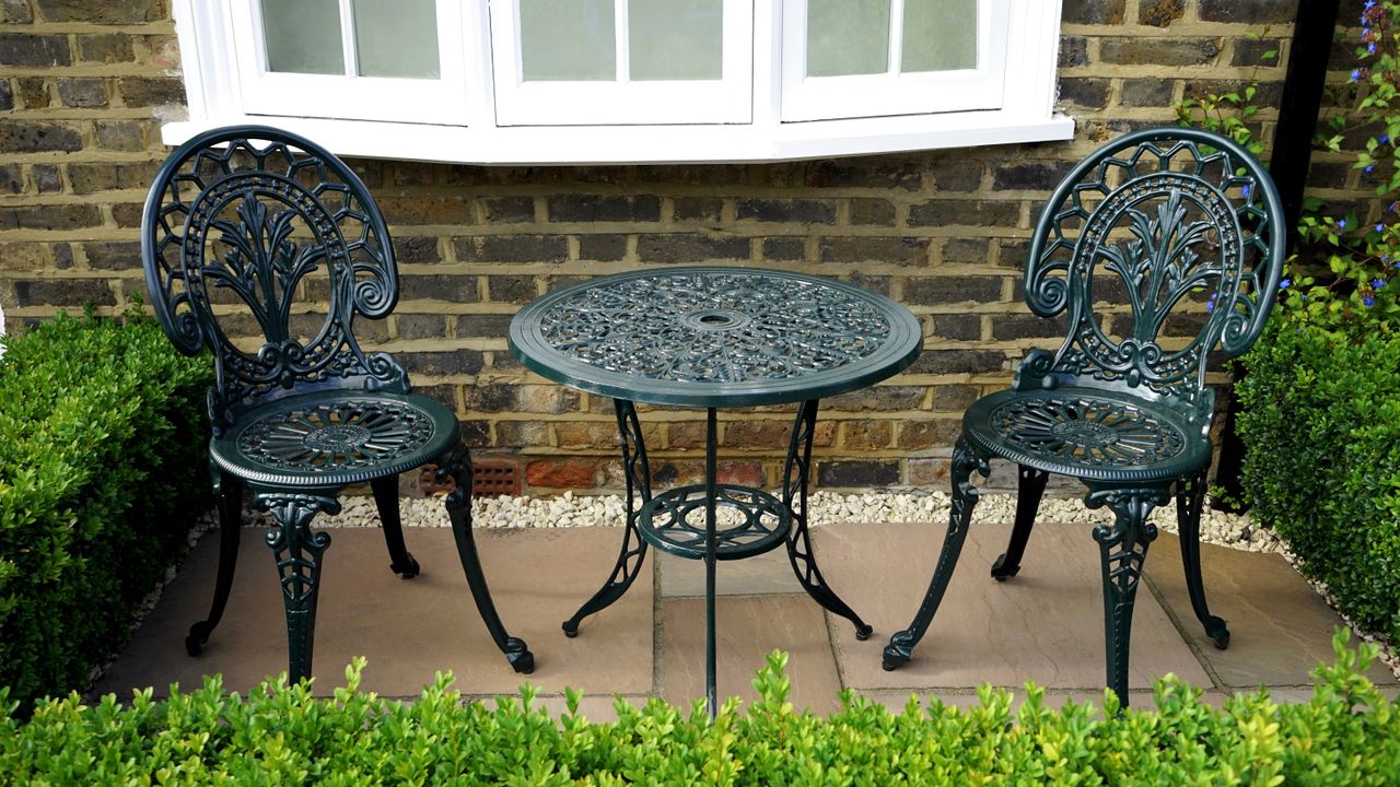 Elegant outdoor garden setting with vintage iron chairs and table beside a brick wall.