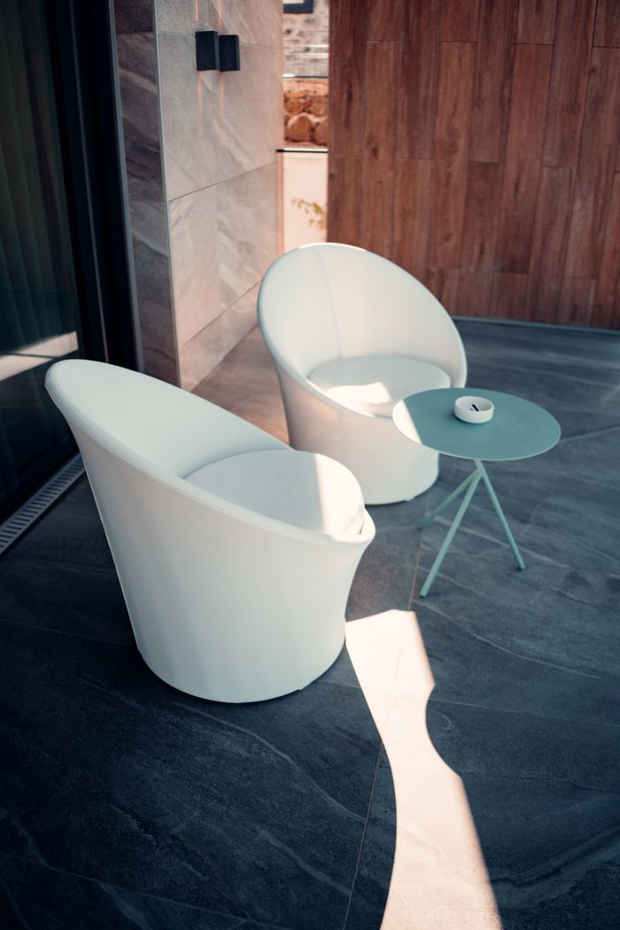 Stylish white chairs and table on an outdoor patio in sunlight.