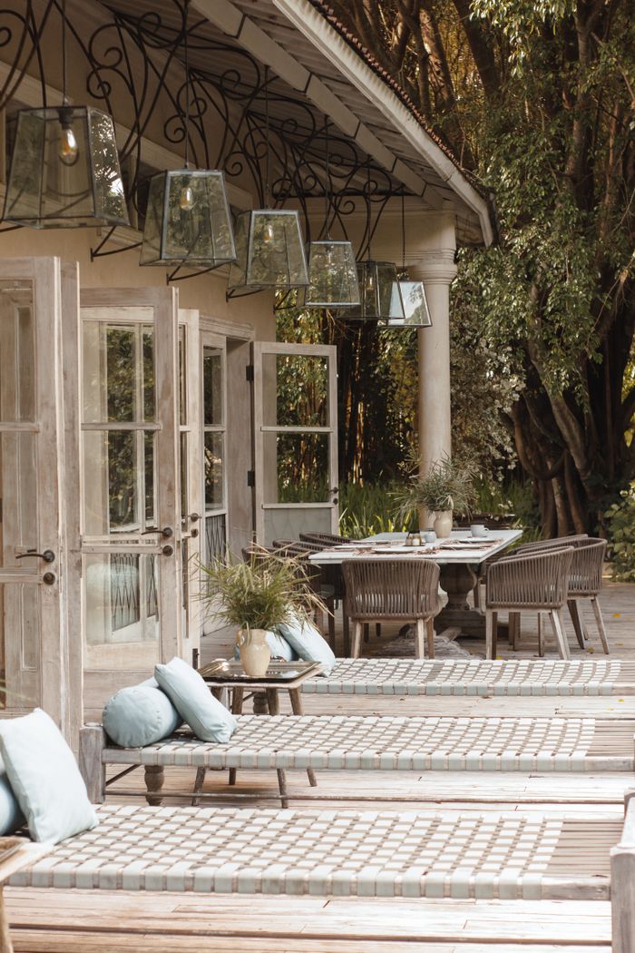 Elegant outdoor seating area with lounge chairs and dining table under a canopy of trees.